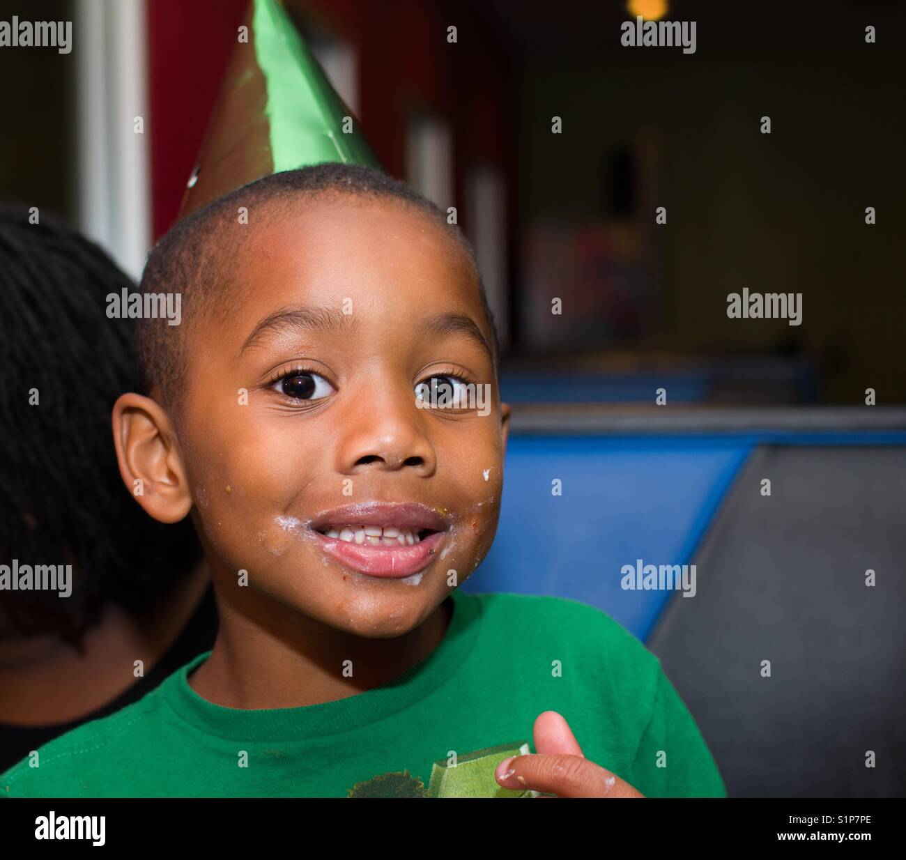Smiling boy at birthday party with birthday hat and messy cake icing