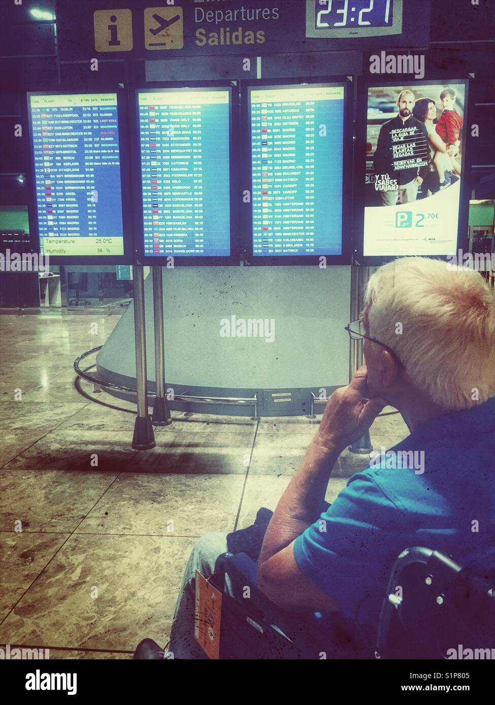 Senior man in a wheelchair, looking at the departure board in El Altet Airport, Alicante, Spain - Smartphone Captured Stock Image