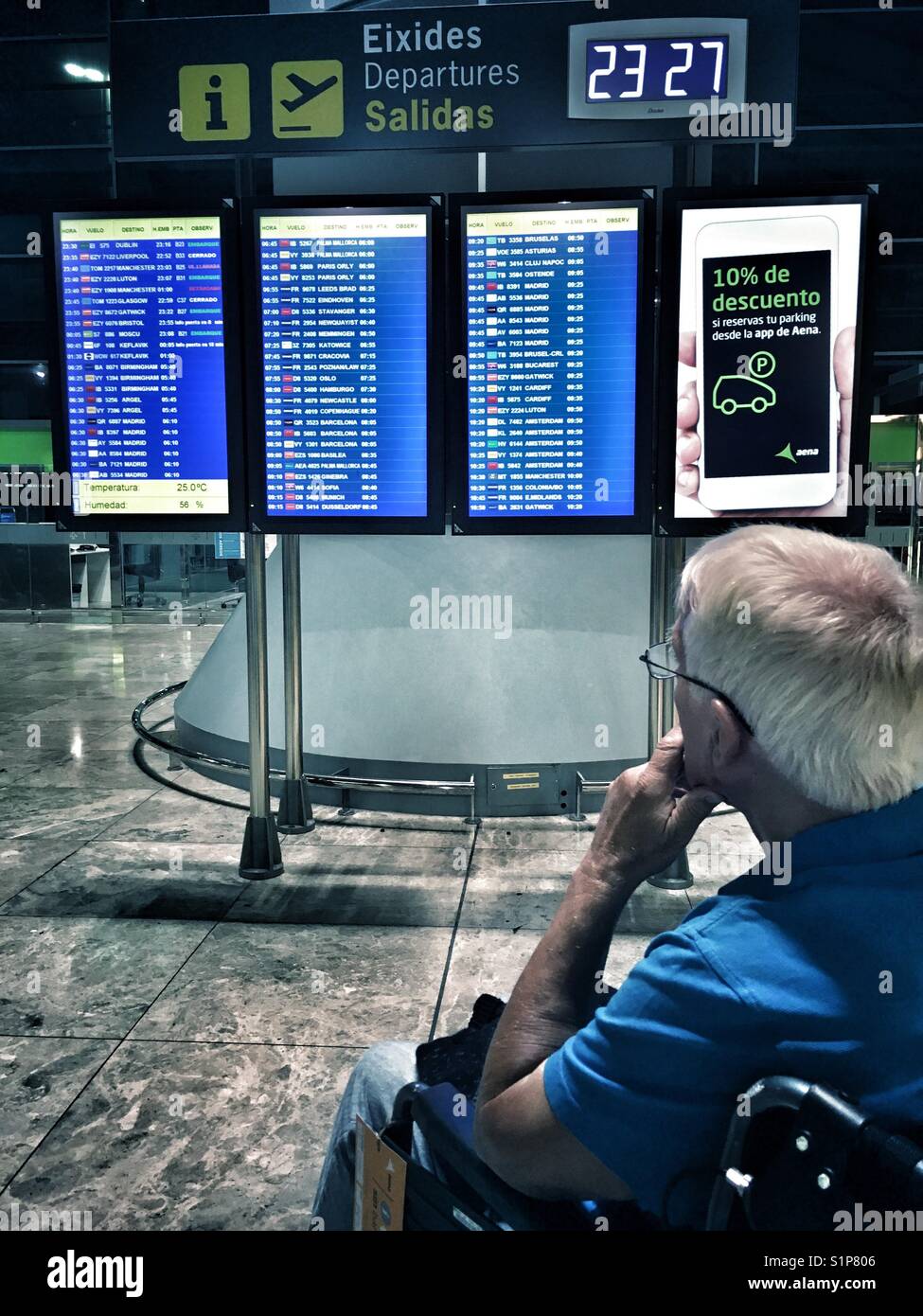 Senior man in a wheelchair looking at the departure board in El Altet airport, Alicante, Spain - Smartphone Captured Stock Image