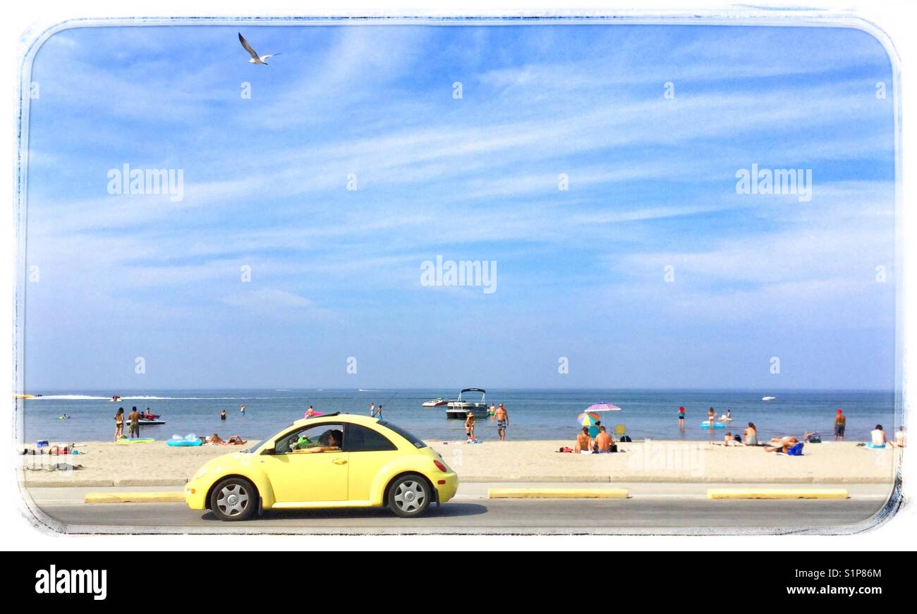 Yellow VW beetle driving along seaside road. - Smartphone Captured Stock Image