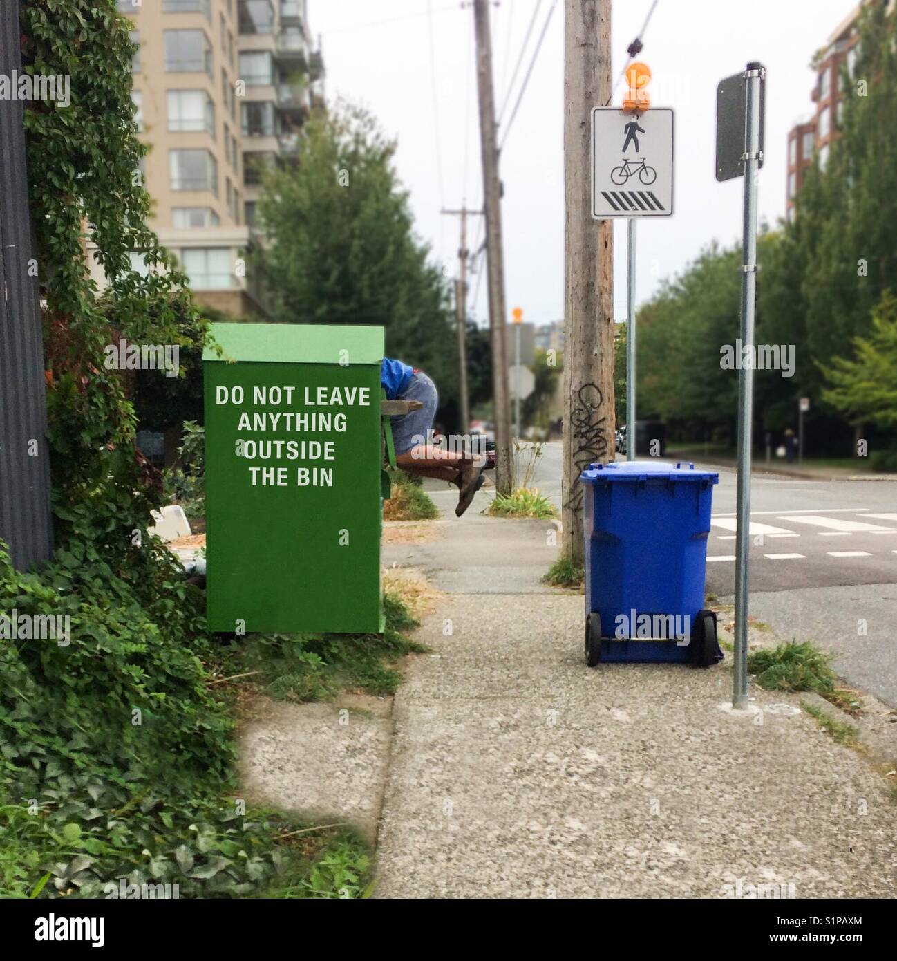Comical capture of a man hanging out of an outdoor clothing bin. - Smartphone Captured Stock Image