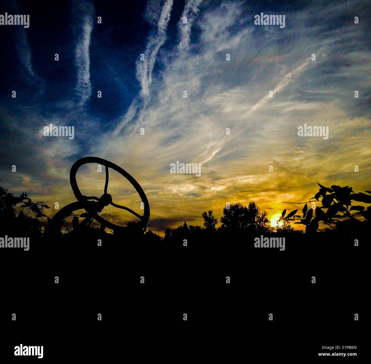 Tractor steering wheel silhouette against blue and gold sunset sky - Smartphone Captured Stock Image