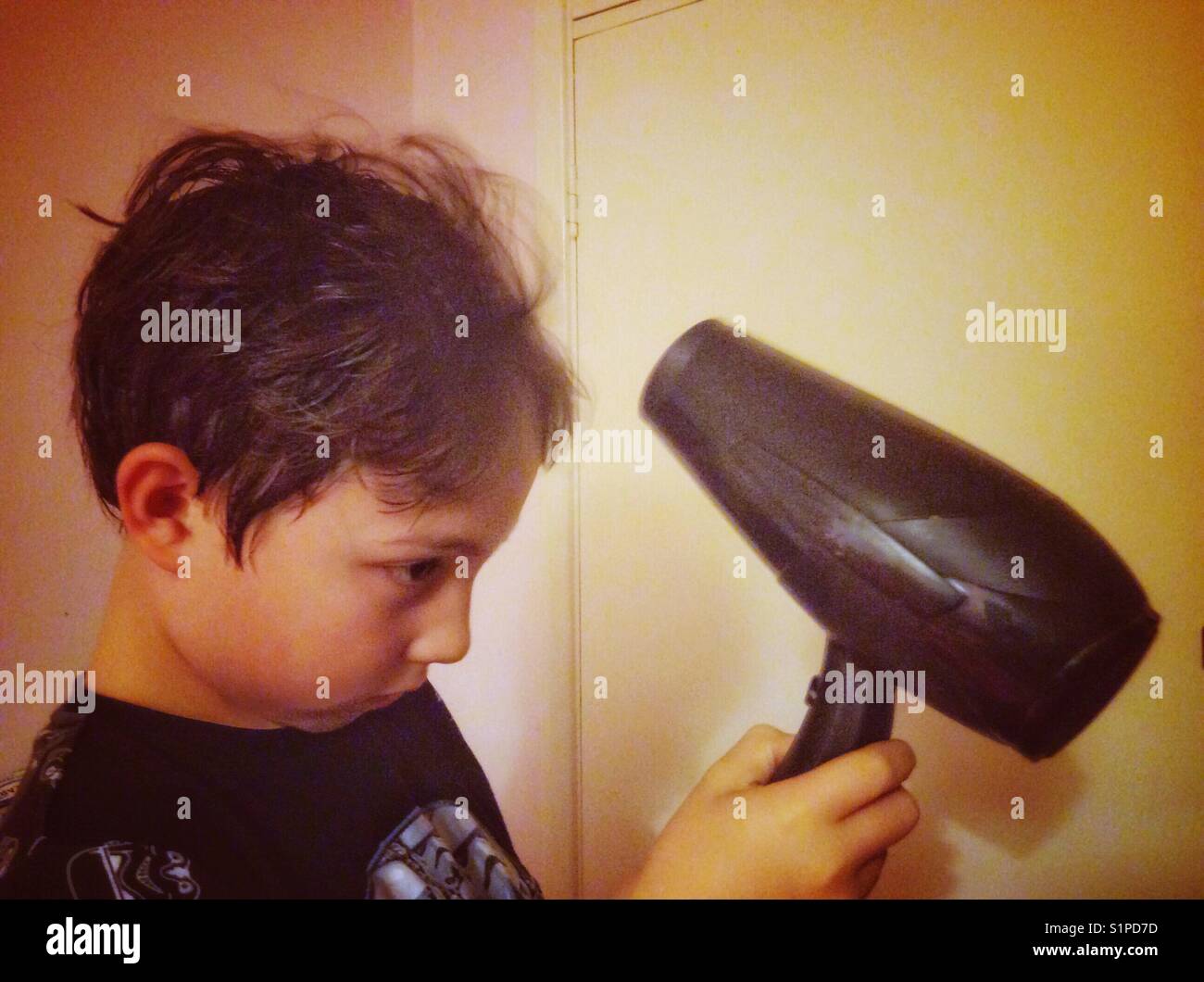 A young boy dries his hair with a hair dryer. Stock Photo