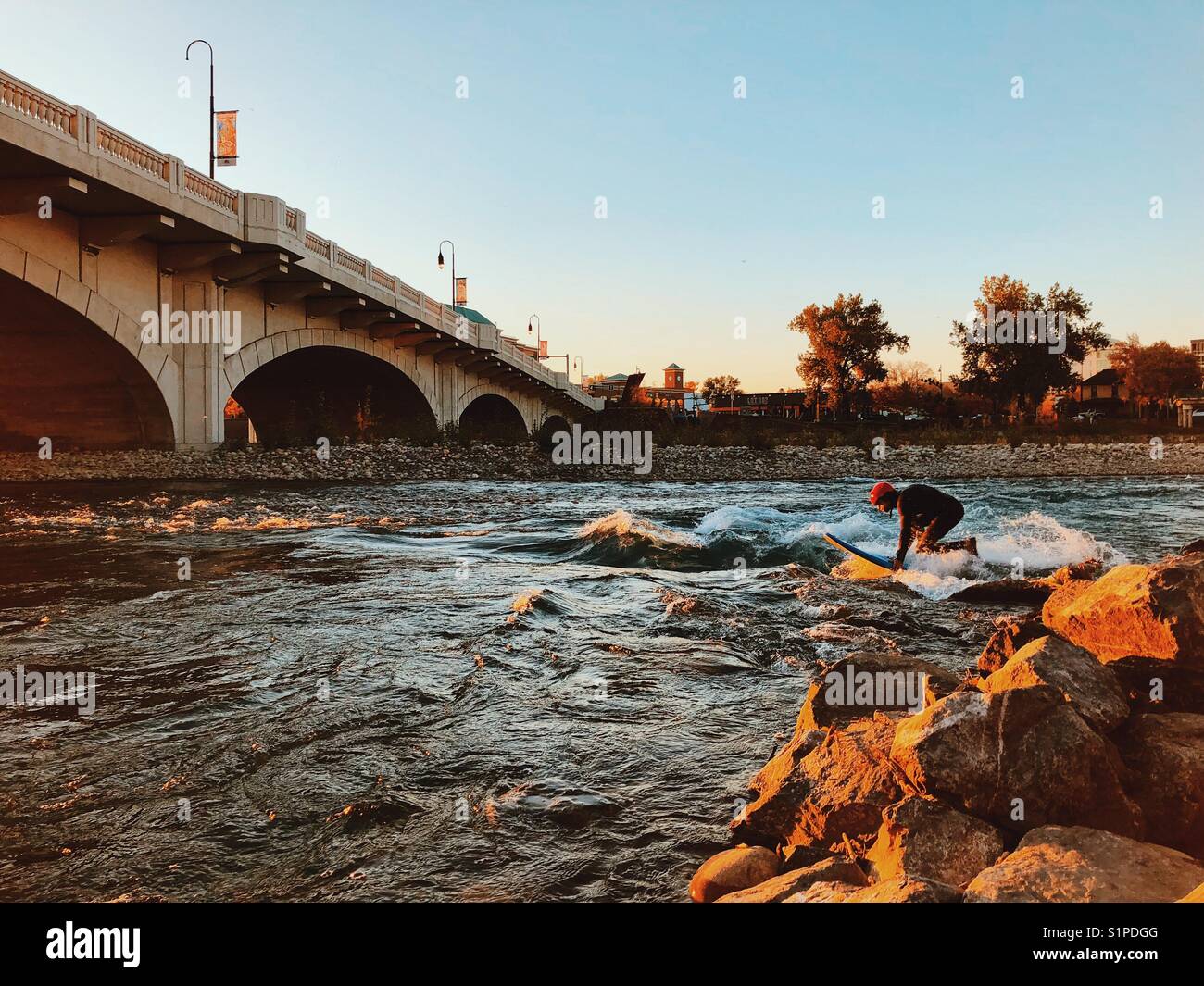 A surfer tries to get up on their board on the Bow River by the 10th St. bridge in Calgary Alberta Canada Stock Photo