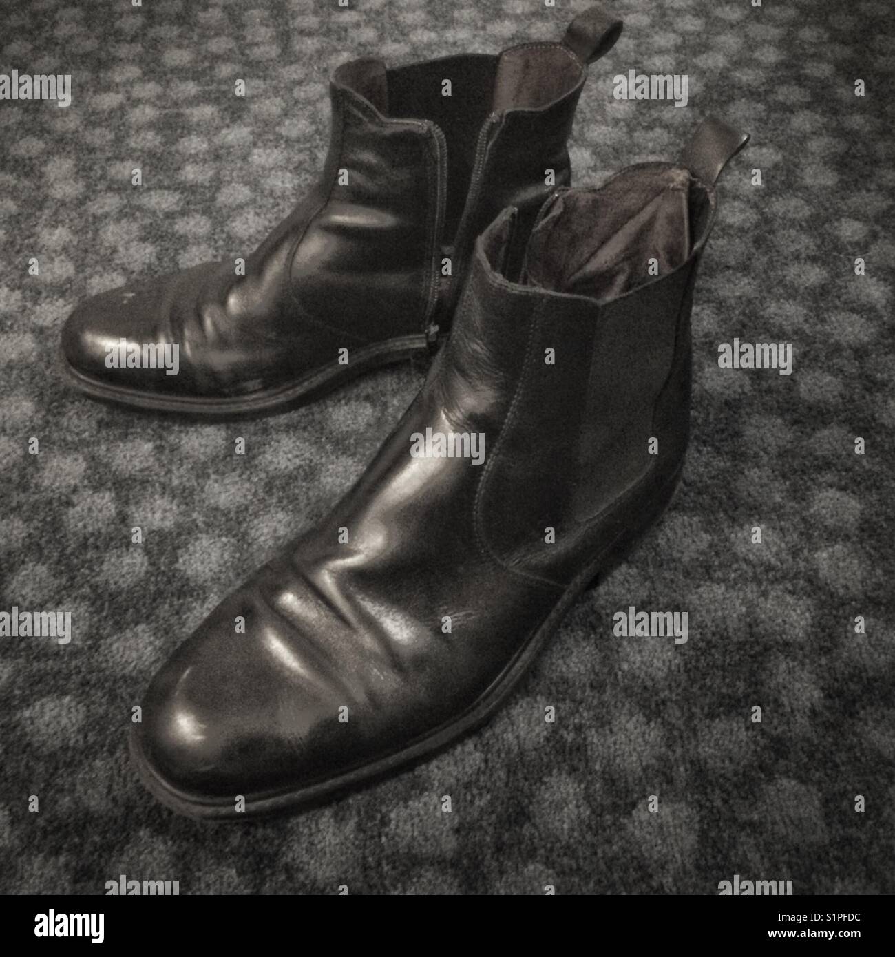 Worn black Chelsea style zip up men’s fashion boots on carpeted floor. Stock Photo