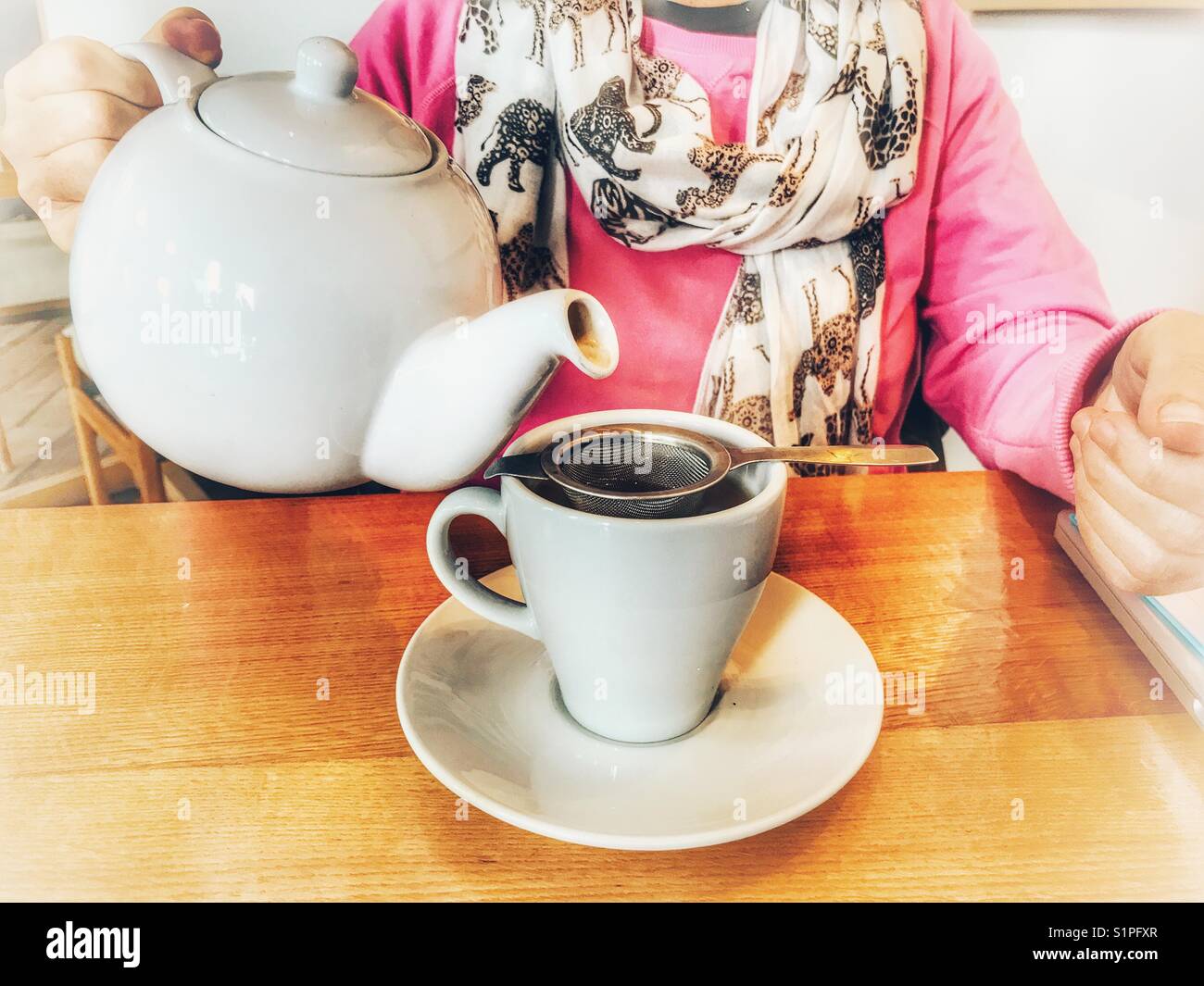 Woman in a restaurant, pouring a cup of tea from a teapot - Smartphone Captured Stock Image