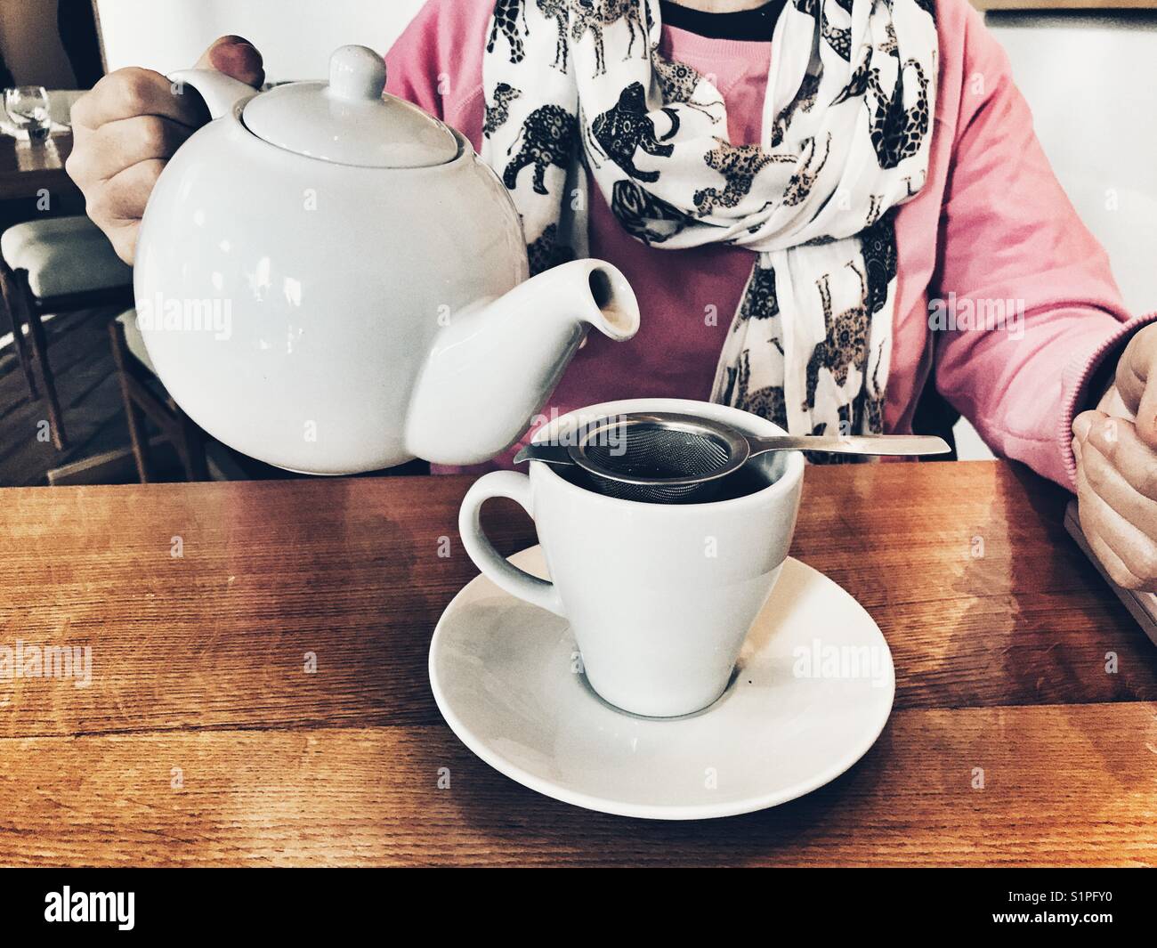 Woman in a restaurant, pouring a cup of tea from a teapot - Smartphone Captured Stock Image