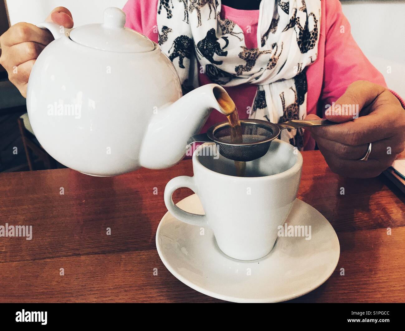 Woman in a restaurant, pouring a cup of tea from a teapot - Smartphone Captured Stock Image