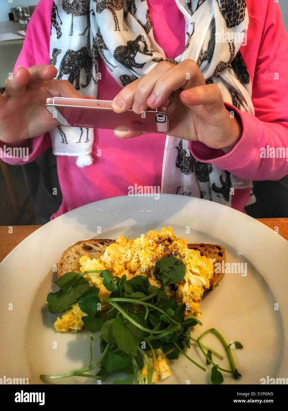 Woman taking a smartphone photo of her breakfast, scrambled eggs on toast - Smartphone Captured Stock Image