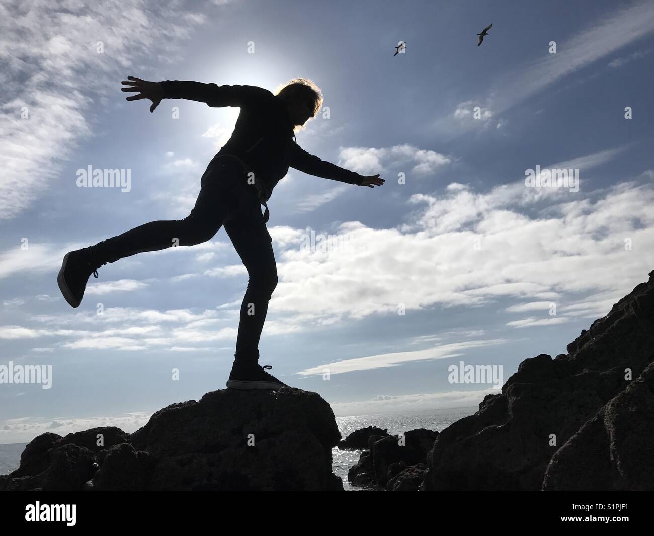 Man balancing on a rock by the seaside - Smartphone Captured Stock Image