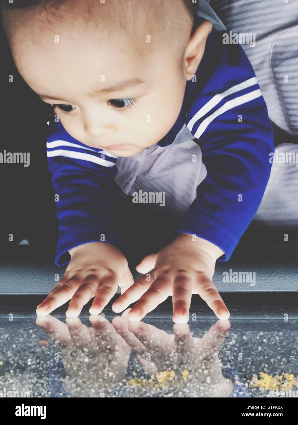 Reflection of cute baby boy's hands on window. Glooming day and raining day concepts. Stock Photo