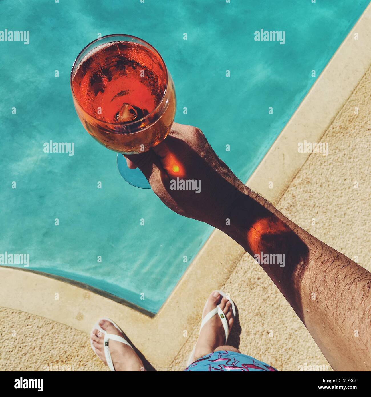 Looking down at man holding glass of Aperol Spritz over swimming pool. - Smartphone Captured Stock Image