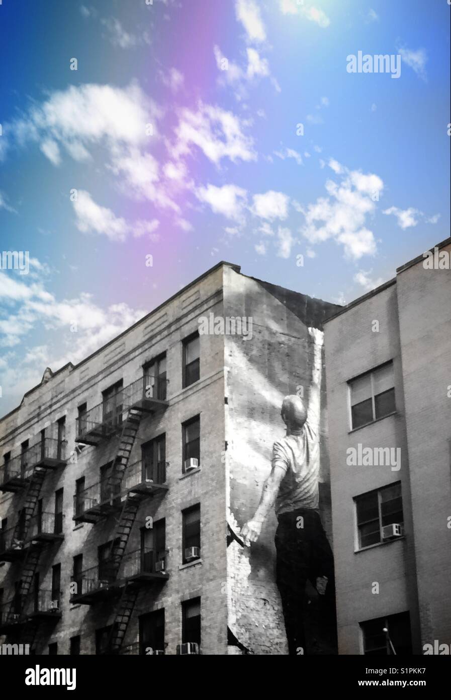 An abstract image of an apartment building in New York City that has a large advertisement on the side of a man reaching up.  A cloudy blue sky with s rainbow can be seen - Smartphone Captured Stock Image