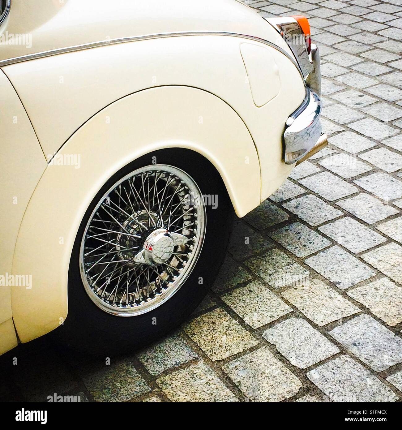 Wheel with wire spokes on Jaguar 3.4 Mark 2 car parked on stone cobbles. - Smartphone Captured Stock Image