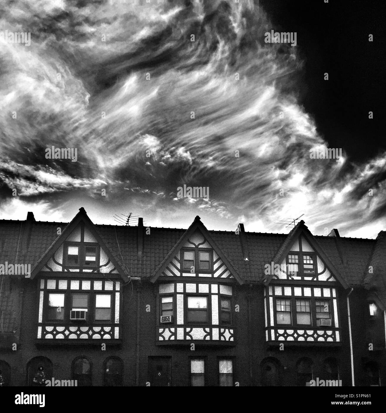 A dramatic black and white image of three Brooklyn brownstones against a dark cloudy sky - Smartphone Captured Stock Image
