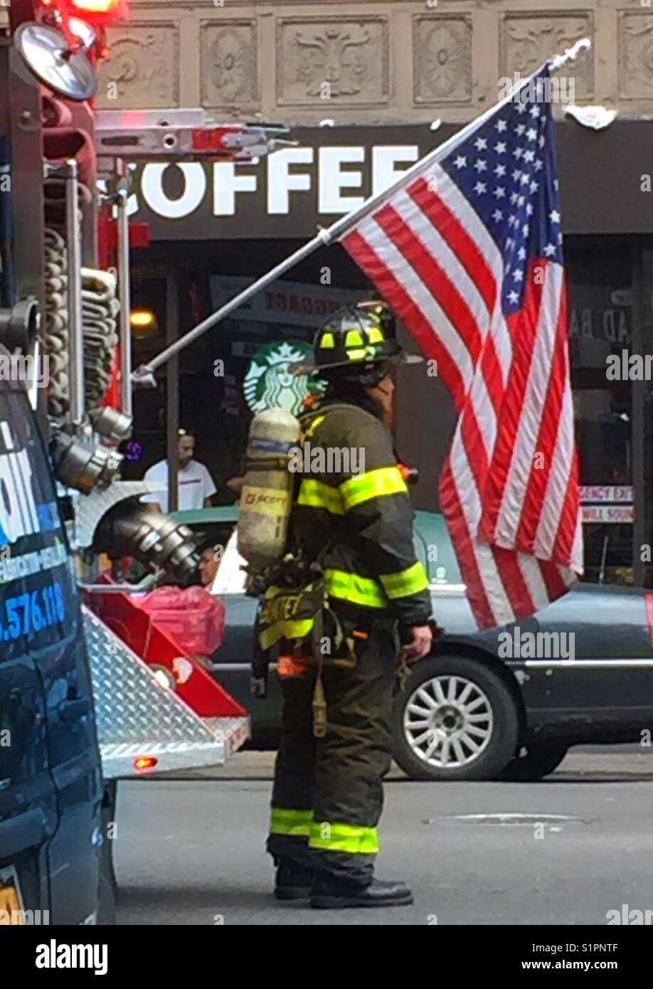 Firefighter with Flag on Fire rig, at post for a fire call, wearing full gear , midtown Manhattan, New York Cuty, Stock Photo