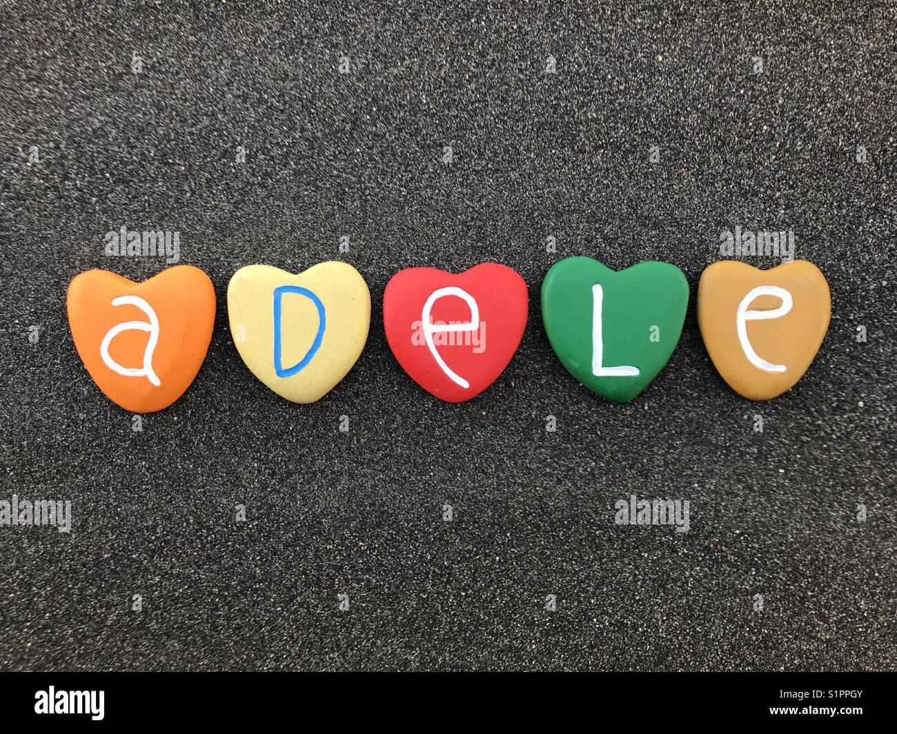 Adele, feminine name with colored heart stones over black volcanic sand Stock Photo