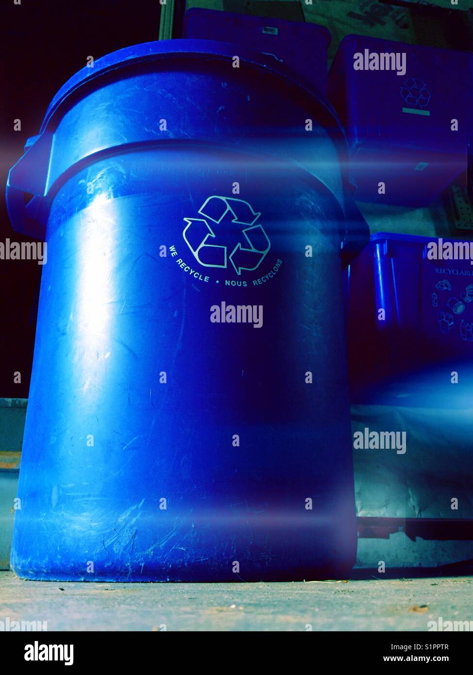 Large recycling bin on a garage floor that says "WE RECYCLE" in English