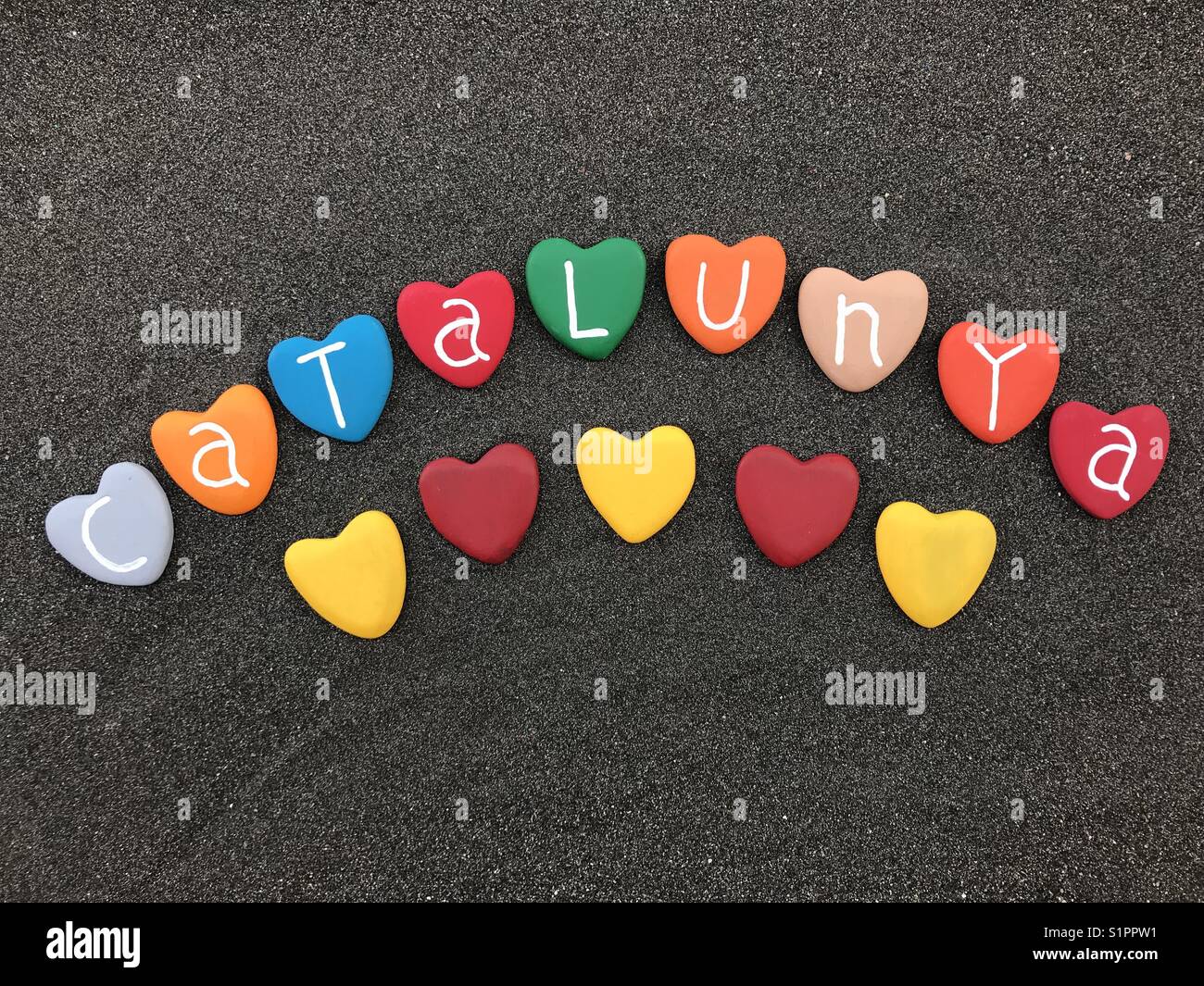 Catalunya with colored heart stones over black volcanic sand - Smartphone Captured Stock Image Catalunya with colored heart stones over black volcanic sand - Smartphone Captured Stock Image