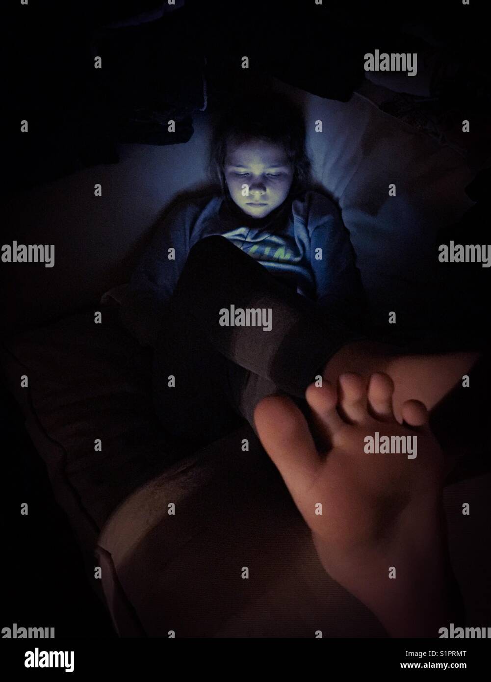 Preteen girl relaxing in dark with her tablet Stock Photo