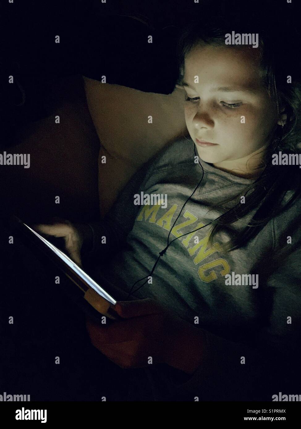 Preteen girl in the dark with her tablet lighting up her face - Smartphone Captured Stock Image