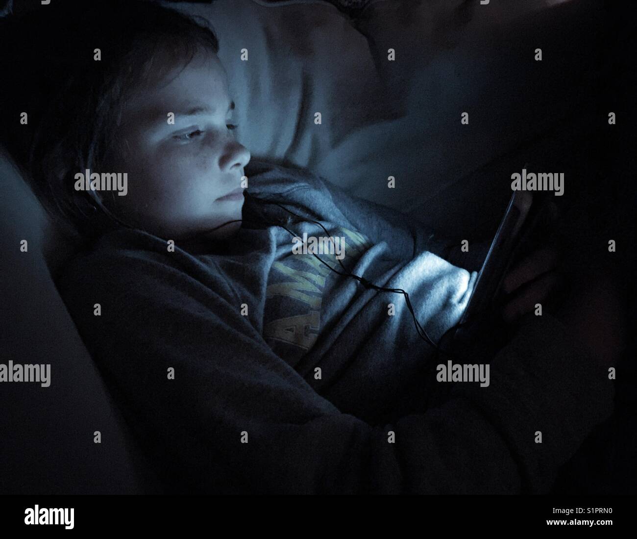 Preteen girl in the dark with a tablet lighting up her face - Smartphone Captured Stock Image