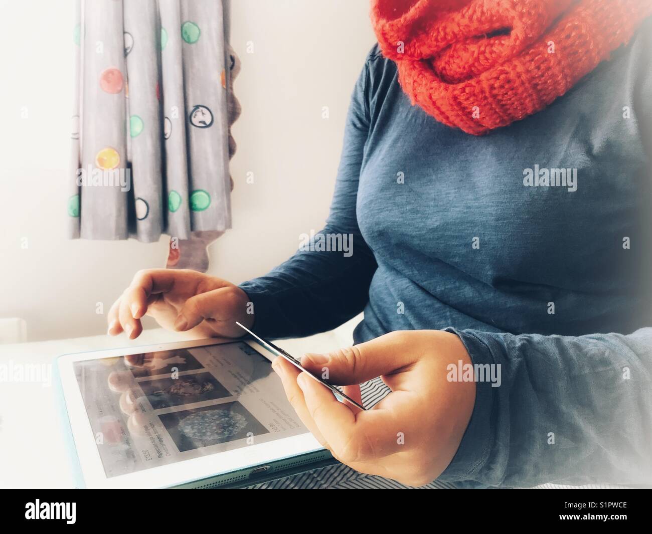 Woman shopping online with a credit/ debit card indoors in winter - Smartphone Captured Stock Image