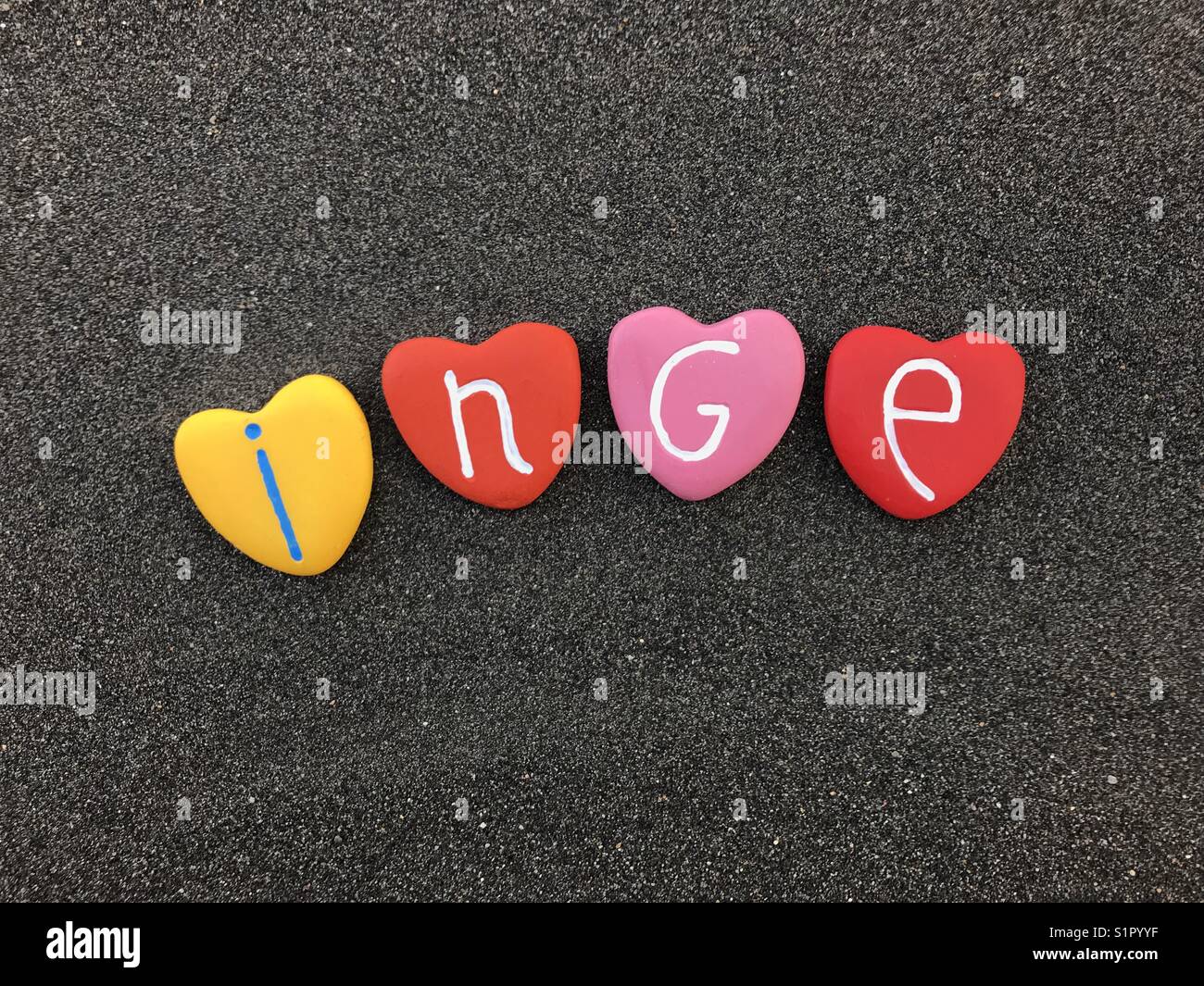 Inge, feminine given name with colored heart stones over black volcanic sand Stock Photo