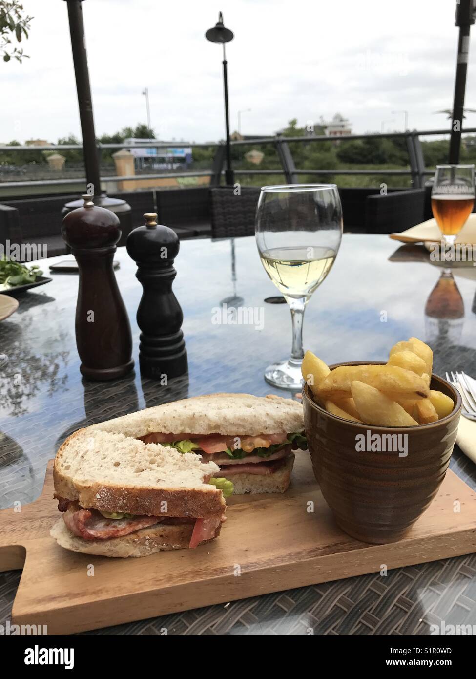 BLT sandwich with a side of chips and a glass of white wine, on a table outside, UK Stock Photo
