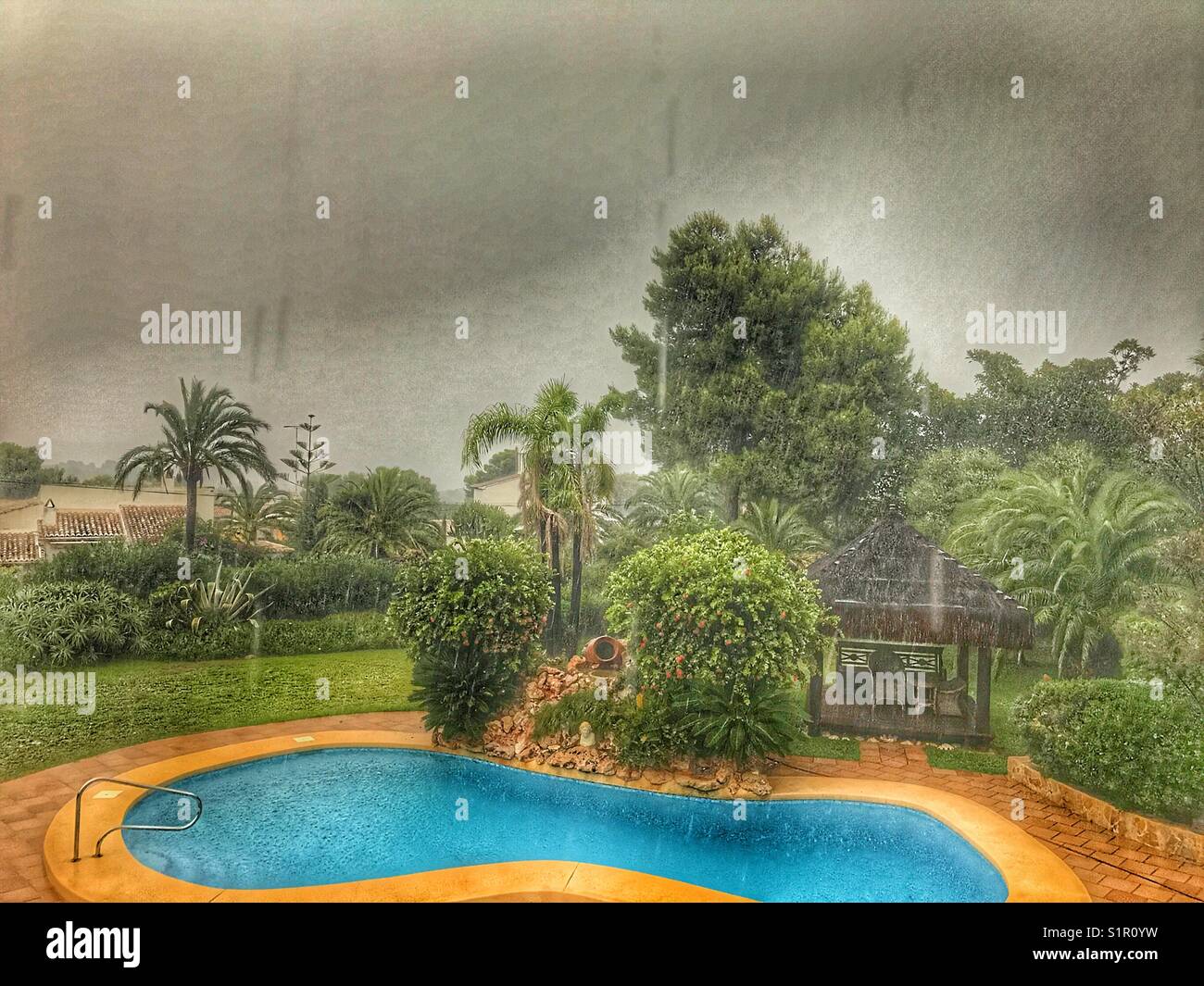 Stormy weather, garden view with swimming pool and heavy rain. Spain
