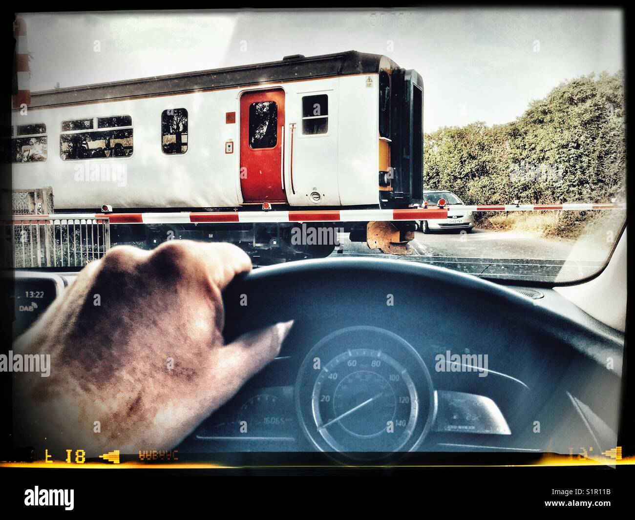 Car driver waiting at a level crossing on the East Suffolk branch line, Melton, Suffolk, UK. - Smartphone Captured Stock Image