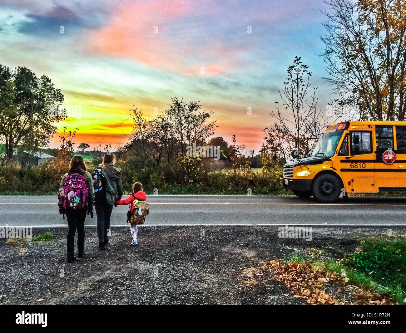 Three girls about to get on school bus in rural Ontario, Canada - Smartphone Captured Stock Image