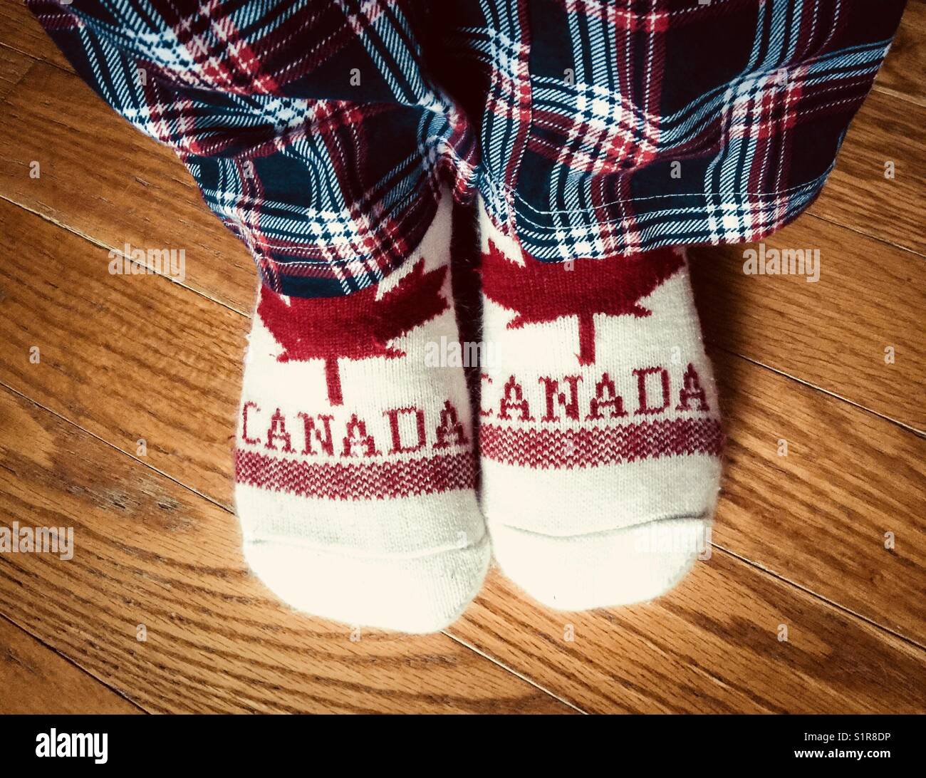 View of flannel plaid pyjama pants and Canada slipper socks being worn by person on hardwood floor Stock Photo