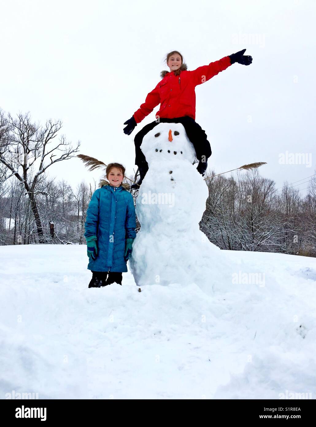 Two girls proudly showing off their newly built snowman in Ontario, Canada - Smartphone Captured Stock Image