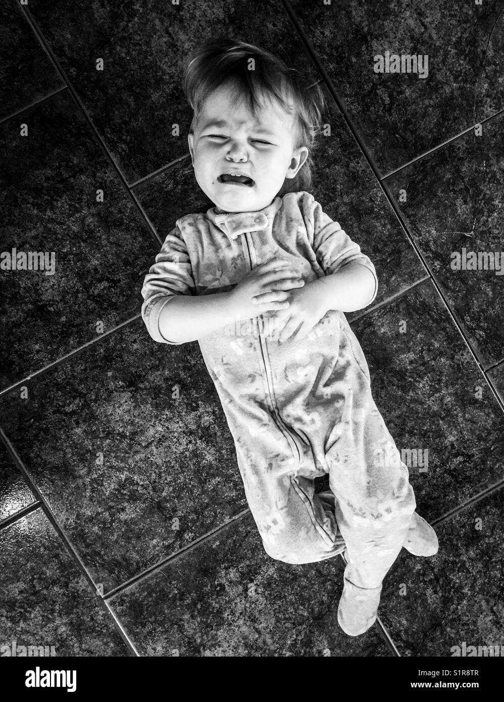 Black and white image of toddler crying on a tile floor Stock Photo