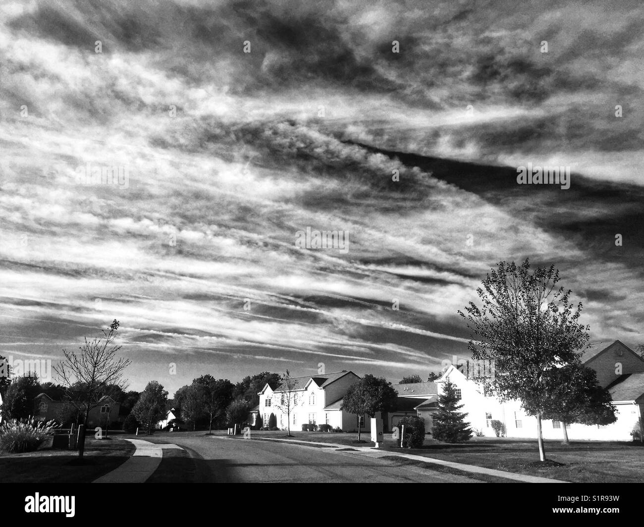 A black and white image of homes in a neighborhood against a dramatic sky with clouds - Smartphone Captured Stock Image
