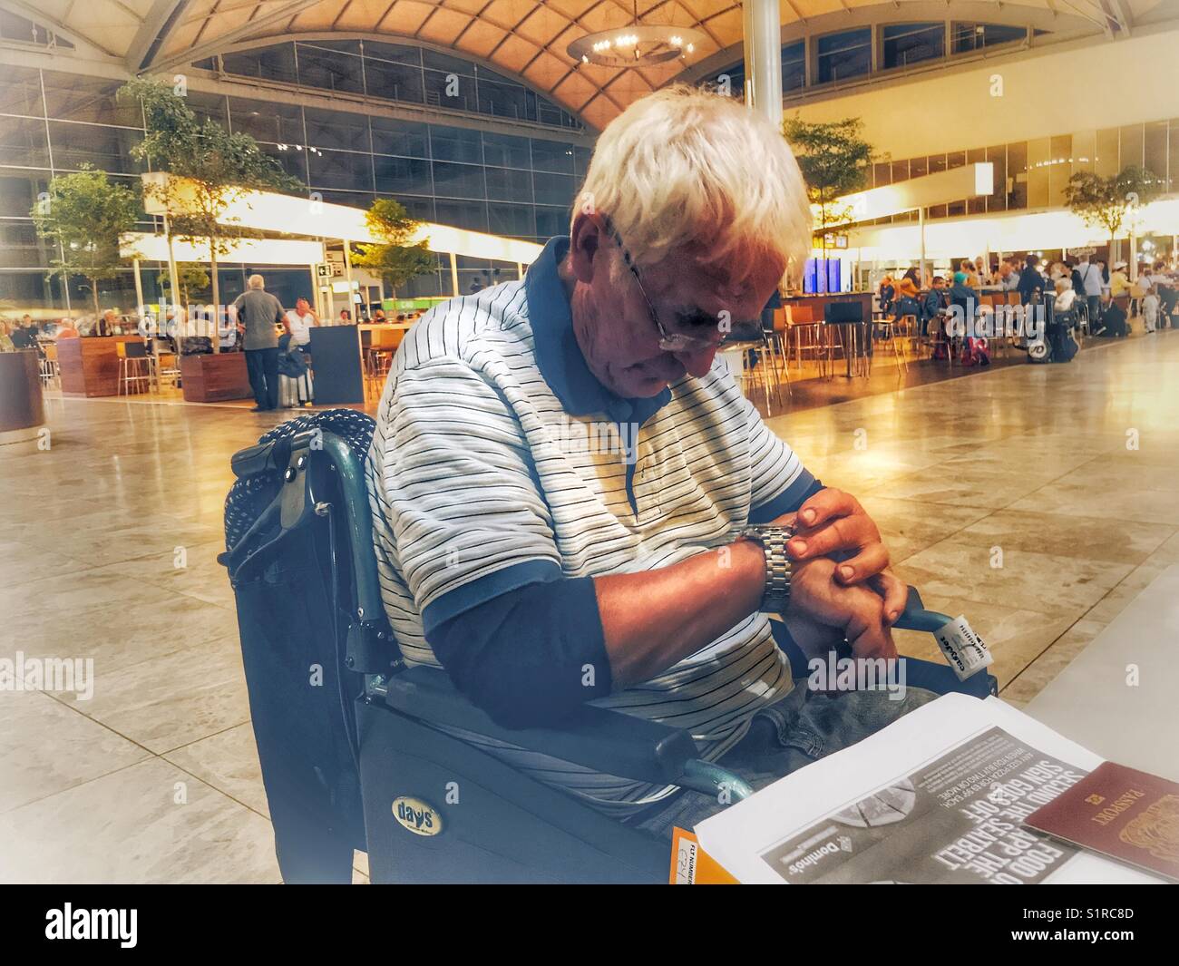 Senior man in a wheelchair looking at his watch, waiting in the departures area of El Altet airport, Alicante, Spain - Smartphone Captured Stock Image Senior man in a wheelchair looking at his watch, waiting in the departures area of El Altet airport, Alicante, Spain - Smartphone Captured Stock Image