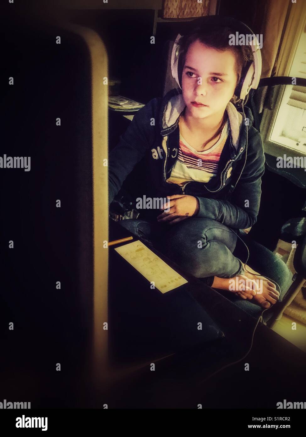 Girl using desktop computer with headphones on in home office - Smartphone Captured Stock Image