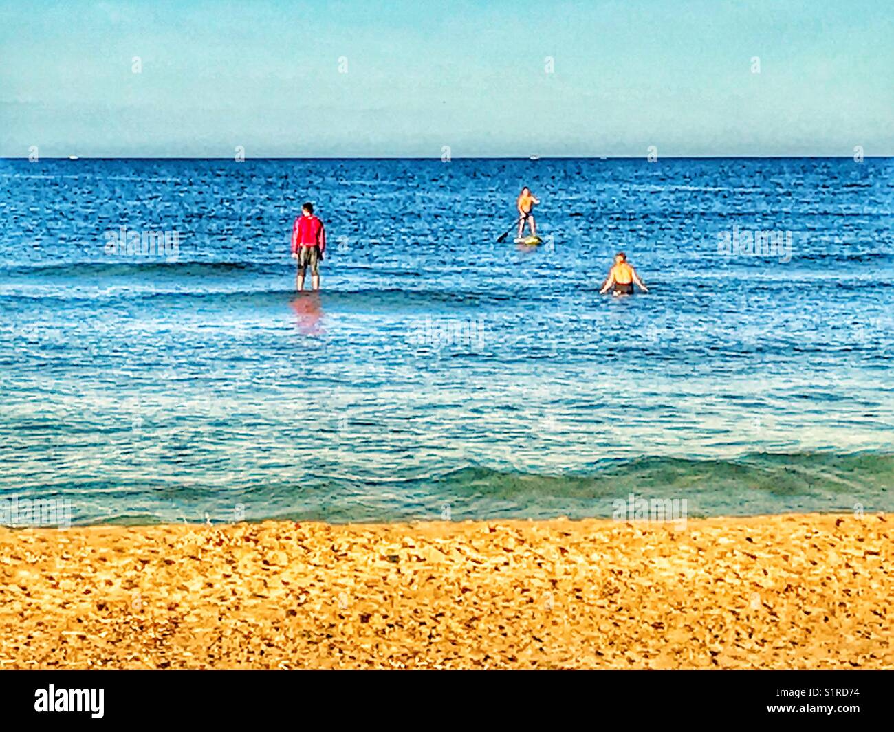 Three people in the sea, including two on paddle boards. Arenal beach, Javea, Alicante, Spain - Smartphone Captured Stock Image
