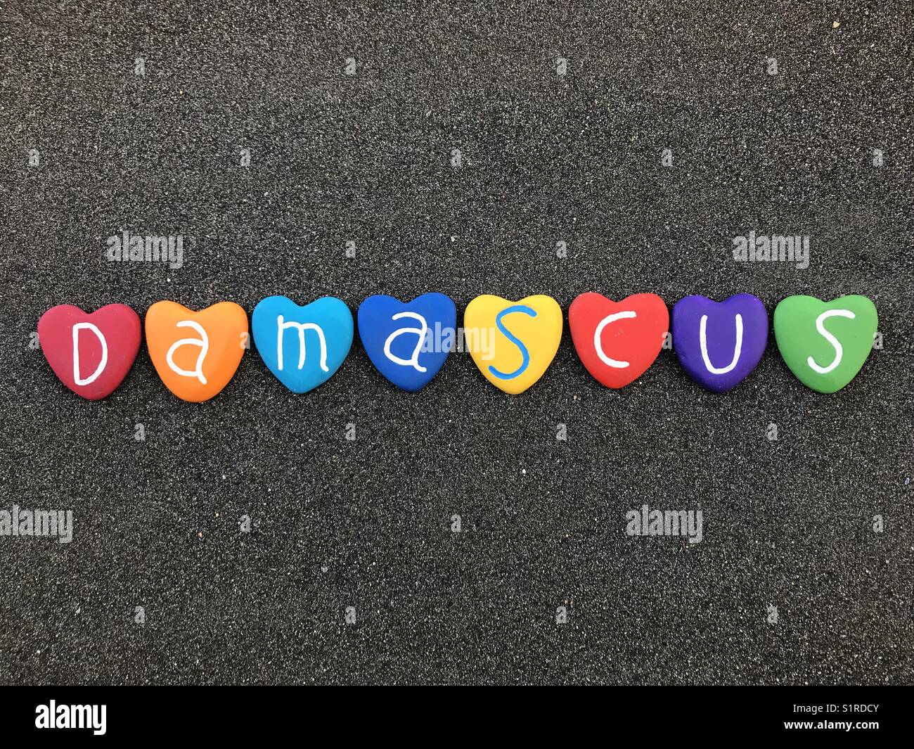 Damascus city name with multicolored heart stones over black volcanic sand - Smartphone Captured Stock Image