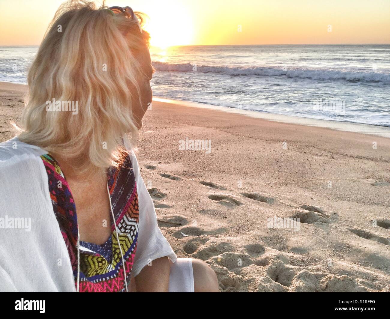 A woman sits on the beach watching the sunrise over the sea. - Smartphone Captured Stock Image