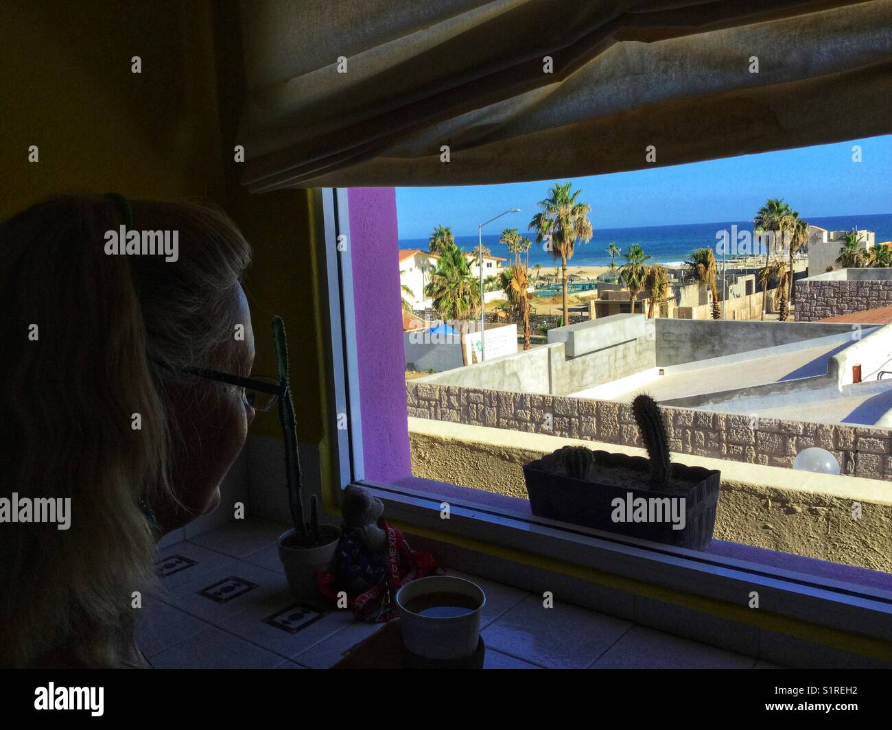 Woman looking out a hotel window towards the sea. - Smartphone Captured Stock Image