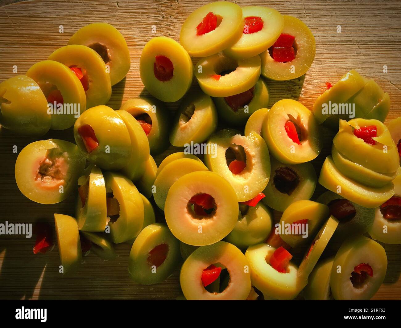 Sliced stuffed green olives on a wooden cutting board lit by the evening sun. - Smartphone Captured Stock Image