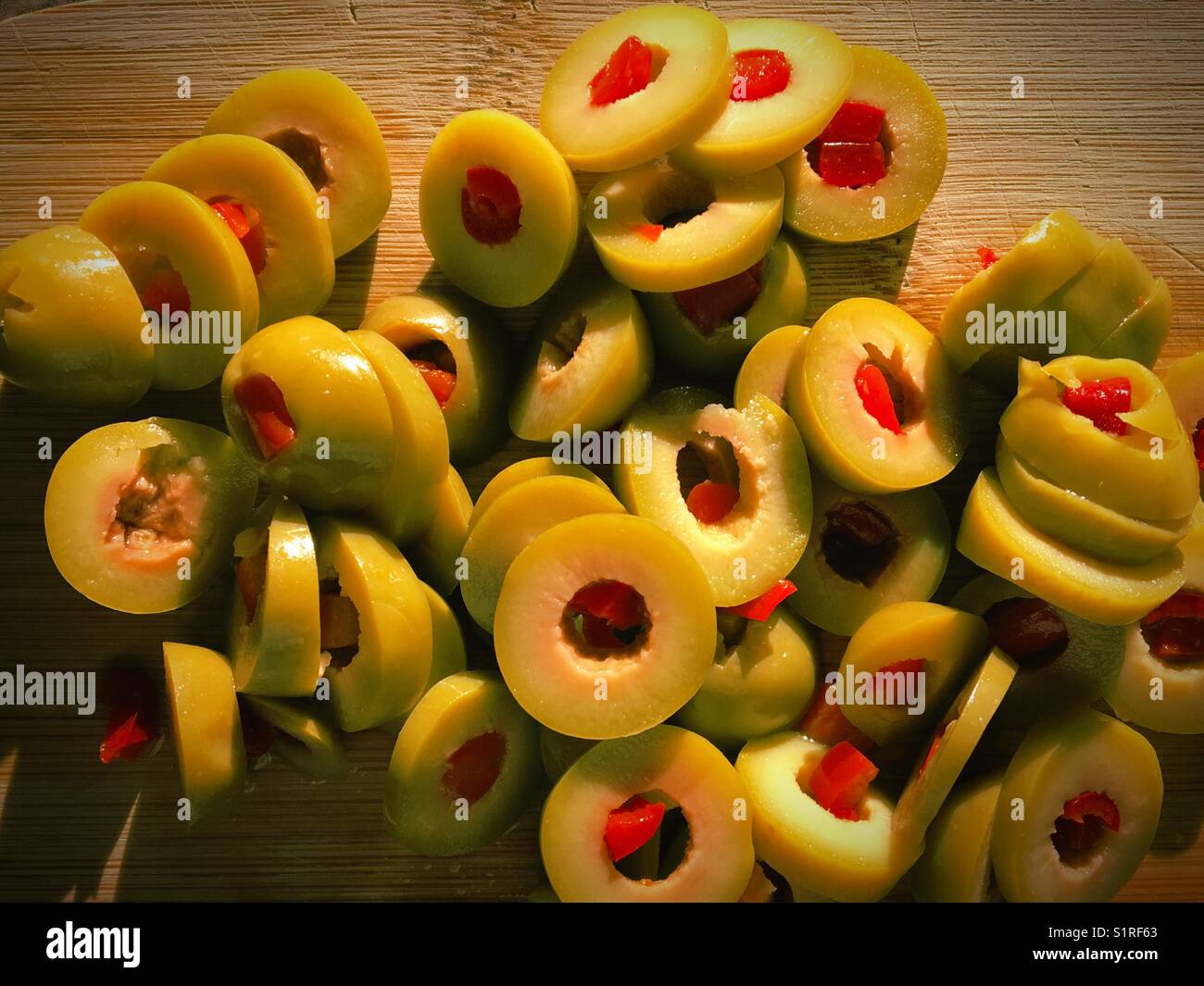 Sliced stuffed green olives on a wooden cutting board lit by the evening sun. Stock Photo