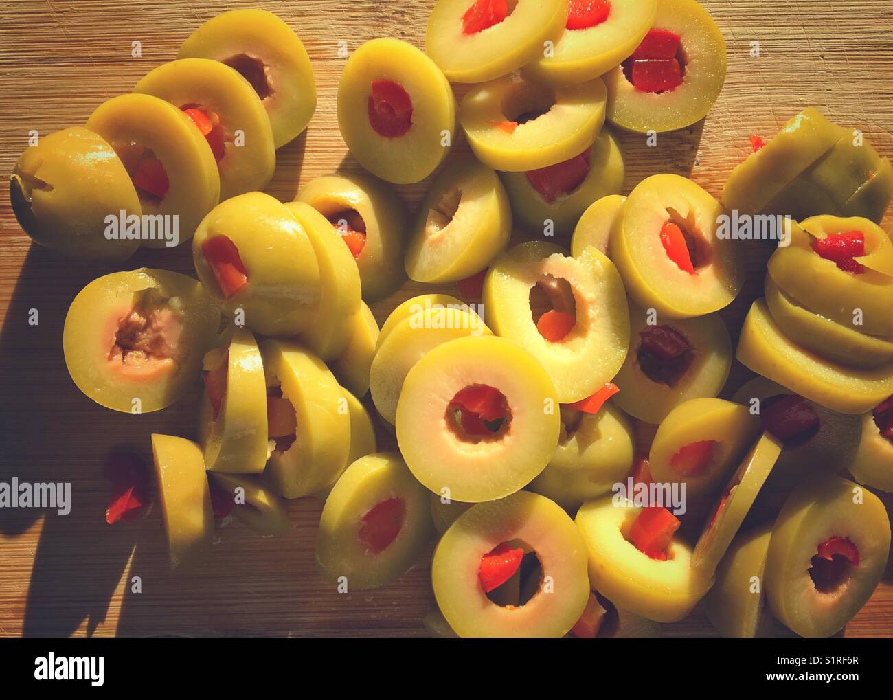Sliced up pimento filled green olives on a wooden cutting board lit up by late afternoon sun. - Smartphone Captured Stock Image