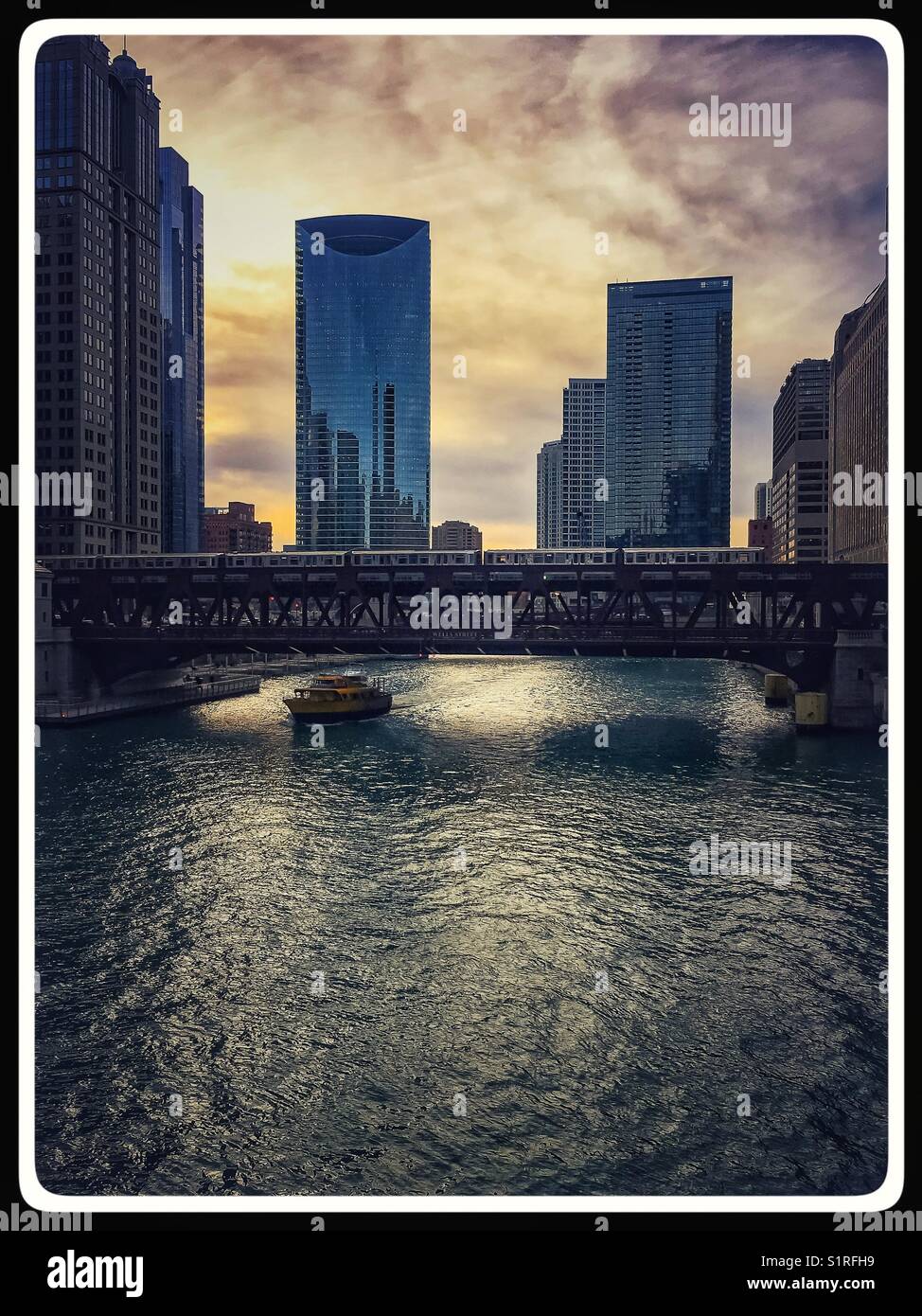 Stunning view of the Chicago River as the sun begins descent and water taxi disappears under a bridge. Stock Photo