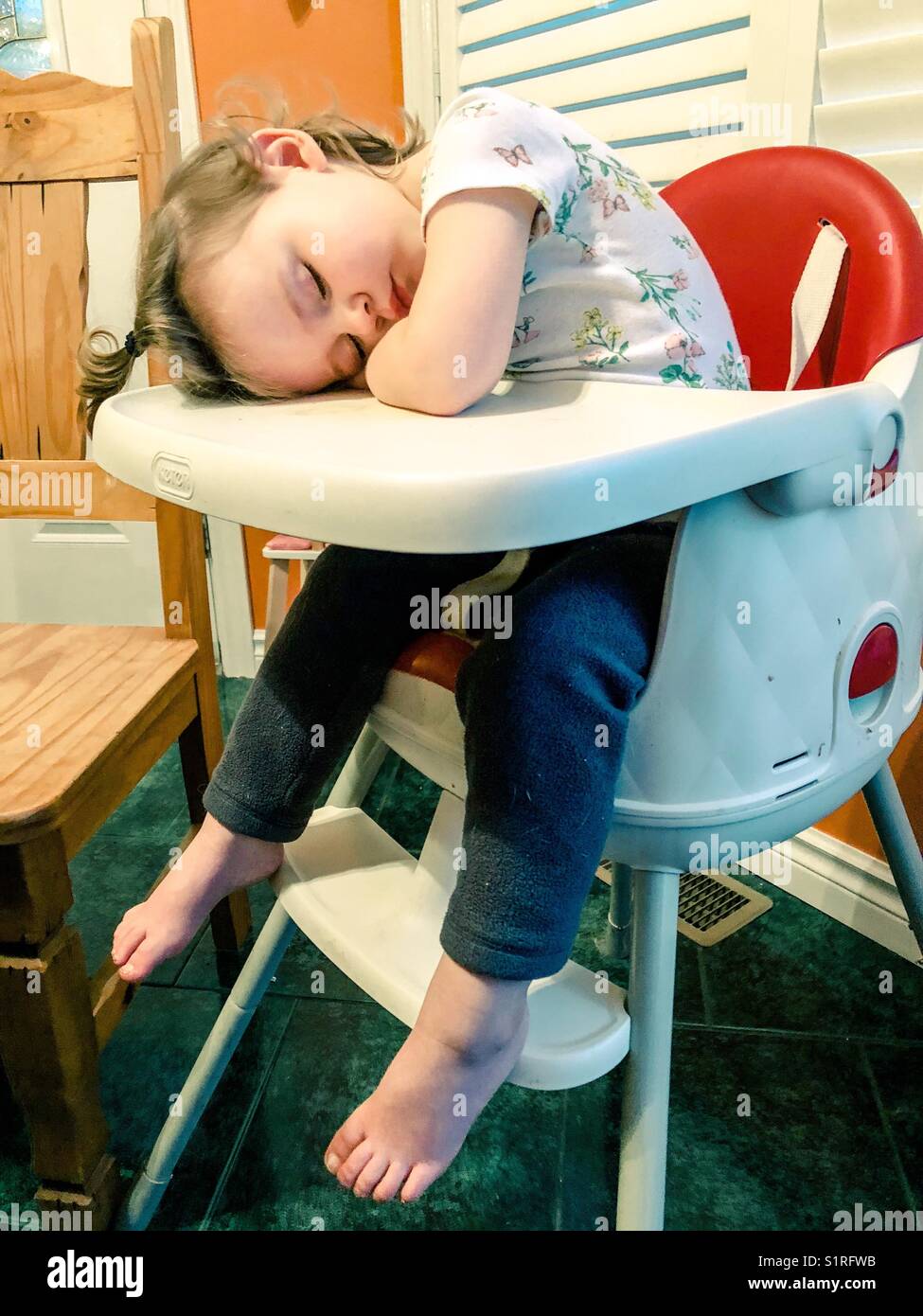 Toddler girl asleep in her high chair at dinner - Smartphone Captured Stock Image