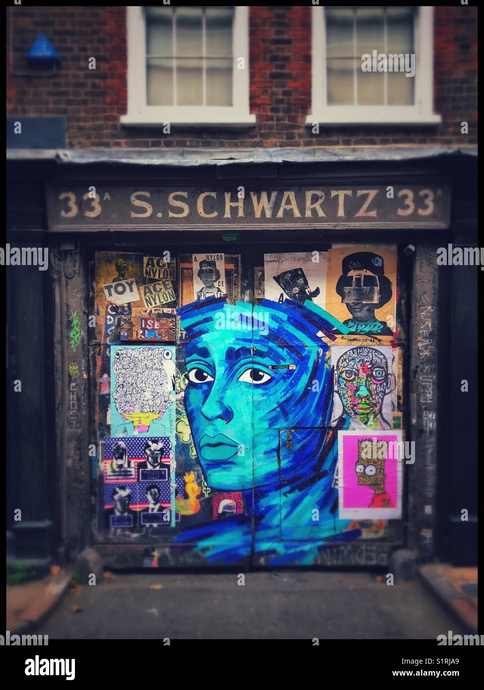Interesting and inspirational graffiti - mostly portraits - adorns the front of a property in the famous Brick Lane area of London, England. A blue portrait is prominent. Photo Credit © COLIN HOSKINS. - Smartphone Captured Stock Image