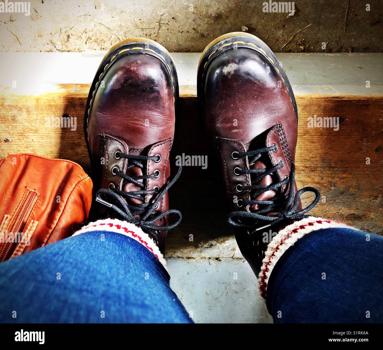 Selfie view of sitting on grungy wooden step wearing brown leather boots, thermal socks and blue skinny jeans - Smartphone Captured Stock Image