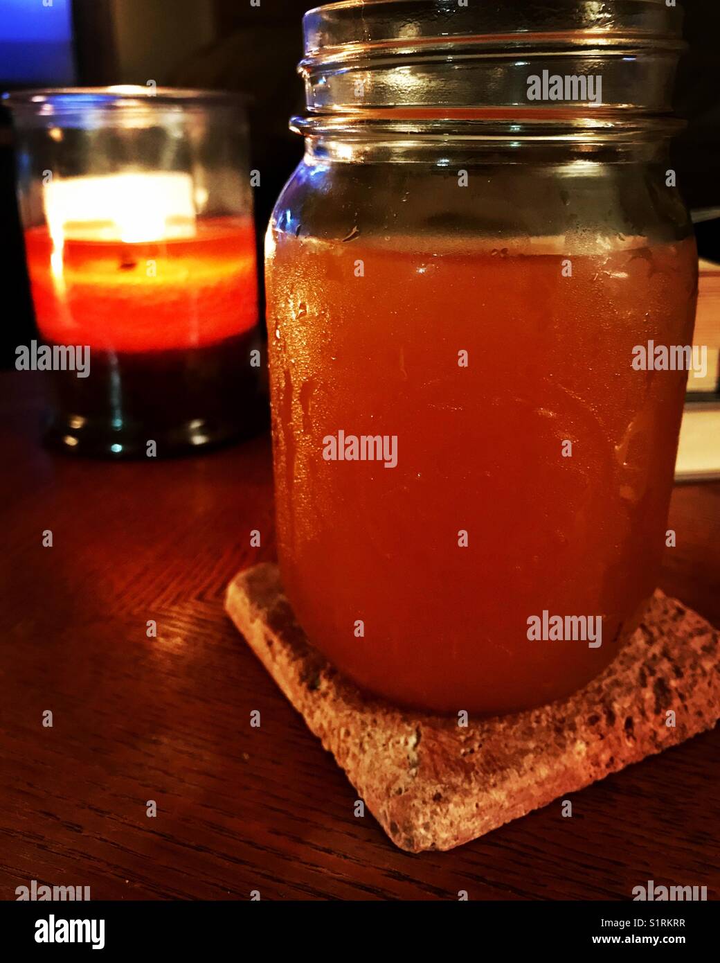 Candle burning behind a mason jar full of apple cider. Stock Photo